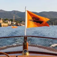 Orange custom burgee flag with boat wave design flying on a pole at the bow of a boat on a lake
