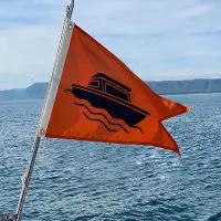 Orange custom burgee flag with a boat silhouette flying on a pole over a lake, showcasing personalized nautical design