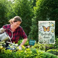 Outdoor backyard scene with a smiling woman and a "Butterfly Diner" custom garden flag among blooming plants