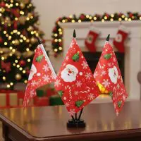 Triple pole Christmas desk flag set displayed on a wooden table with festive holiday decorations in the background.