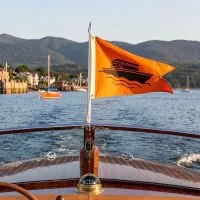 Orange custom burgee flag with boat wave design flying on a pole at the bow of a boat on a lake