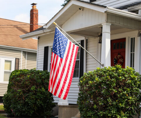 American flag hanging proudly on the front porch of a suburban home