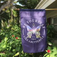 Custom purple butterfly garden flag with "Your Text Here" design, displayed outdoors among green plants